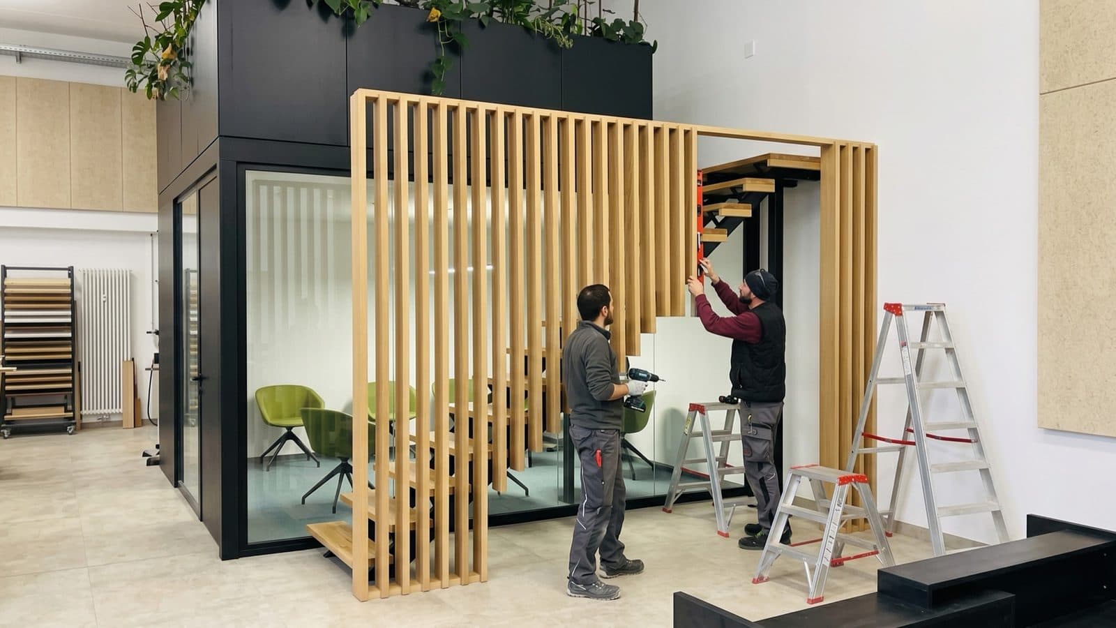 Zwei Monteure von Fast Systemmöbel bauen mit Akkuschrauber und Wasserwaage eine Holzlamellenwand an einer Treppe ein